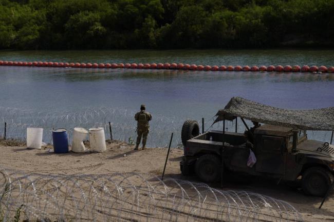 FILE - A guardsman keeps watch over a section of the Rio Grande that is fortified with co<em></em>ncertina wire and large buoys being used as a floating border barrier on the Rio Grande, Aug. 1, 2023, in Eagle Pass, Texas. A federal judge on Wednesday, Sept. 6, ordered Texas to move a large floating barrier to the riverbank of the Rio Grande after protests from the the U.S. and Mexican governments over Republican Gov. Greg Abbott’s latest tactic to stop migrants from crossing America’s southern border. (AP Photo/Eric Gay, File)